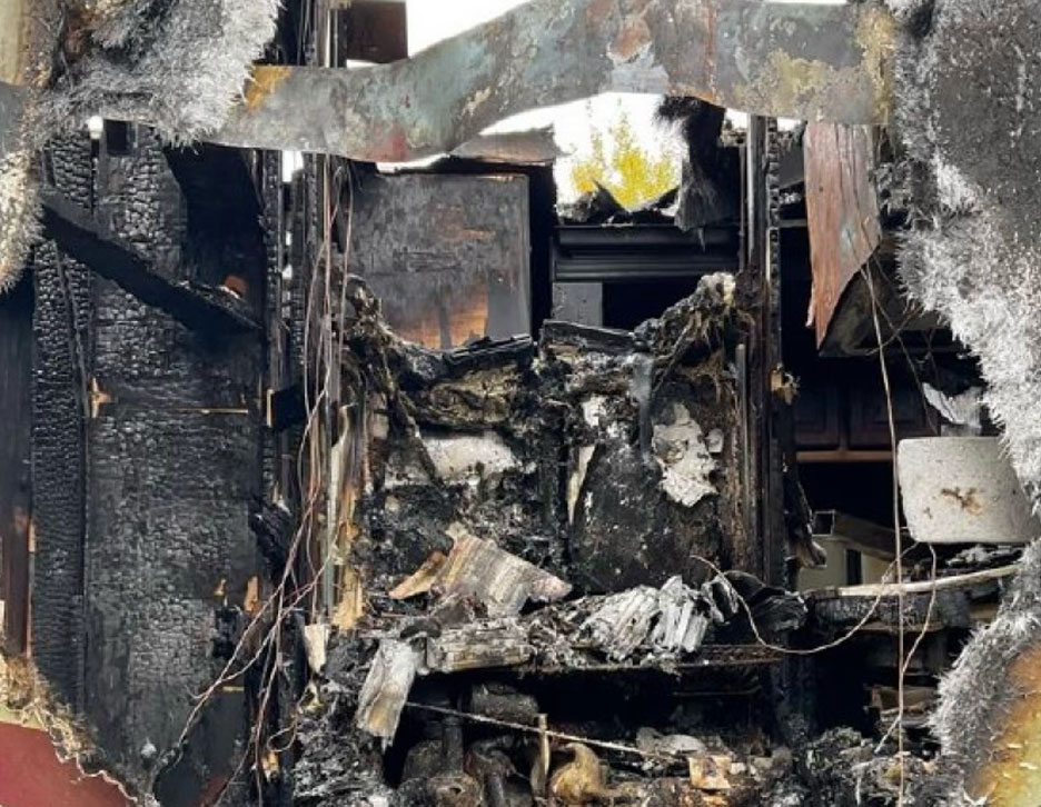 A severely charred interior of a vehicle or equipment cabin, showing extensive fire damage to the dashboard, steering column, and surrounding structural panels, indicative of a localized origin and cause investigation.