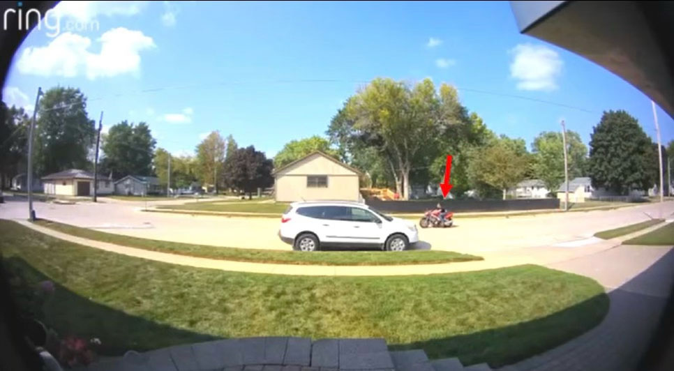 A motorcycle is captured on a Ring doorbell camera, with a red arrow pointing toward it to highlight its position on the street.