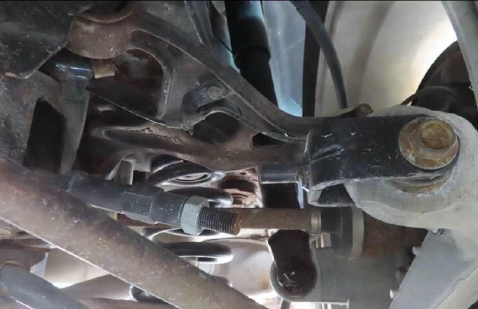 A close-up view of a vehicle's suspension and drivetrain components, showing a damaged lower control arm, a bent tie rod, and an exposed coil spring, consistent with impact damage from a single-vehicle collision.