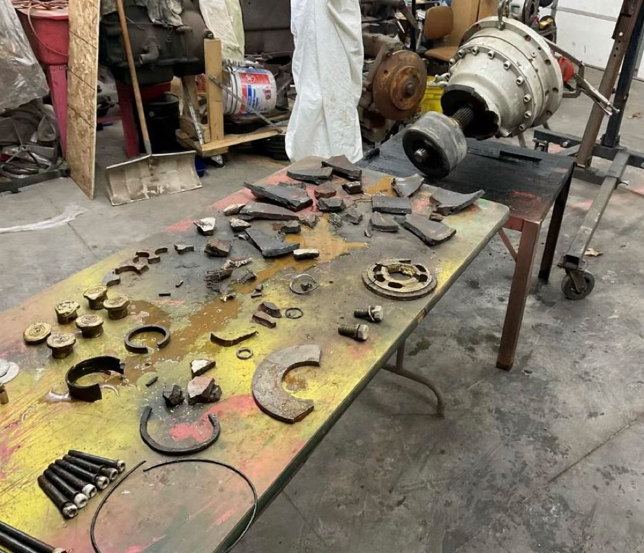 A workbench covered in various disassembled mechanical engine components, including gears, bolts, and metal fragments, organized for a forensic mechanical failure investigation